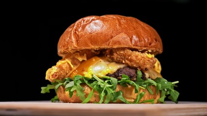 Craft burger is cooking on black background. Consist: sauce, arugula, tomato, red onion rings...