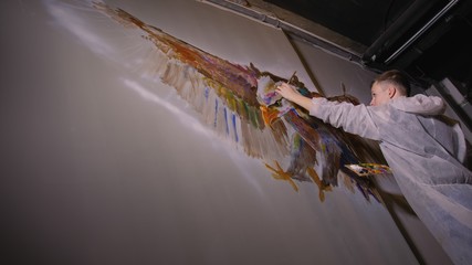 Artist designer draws an eagle on the wall. Craftsman decorator paints a picture with acrylic oil color. Painter painter dressed in a paint coat. Indoor. Dark magic cinematic look.