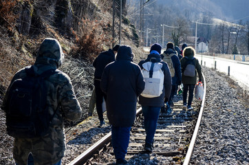 Group of migrants walking along railway tracks. Balkan route. Rear view of men walking on railway...