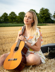 Junge Frau mit Gitarre sitzend auf einen Strohbund