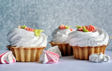 Cake with whipped cream and meringue. White, slightly grayish background. White green rose cream. Tartlet-shaped cake. Cake decorated with cream flowers 