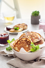 Homemade classic American pancakes with red berry jam, yogurt and herbal tea against window in the morning sun light. Healthy breakfast.