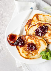 Pancakes with red berry jam and mint, light grey stone background. American cuisine. Breakfast. Top view.