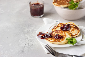 Pancakes with red berry jam and mint, light grey stone background. American cuisine. Breakfast. 