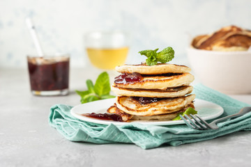 Pancakes with red berry jam and mint, herbal tea. American cuisine. Perfect idea for breakfast. Light grey stone background.