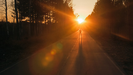 Training an athlete on the roller skaters. Biathlon ride on the roller skis with ski poles, in the helmet. Beautiful sunset silhouette. Autumn workout. Roller sport. Adult man riding on skates.