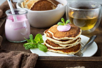Wooden tray with pancakes, yogurt, herbal tea and mint for perfect breakfast. American cuisine.
