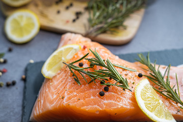 Close up view of raw salmon fillet with herbs and lemon.  Wooden table on the background.