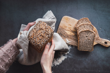 Woman's hands holding a loaf of buckwheat bread with chia. Top view.