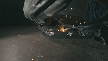 Forge workshop. Smithy. Worker in a welding hood helmet welds a part by electric welding. Sparks are reflected in the protective screen. Blacksmith makes iron product for manufacture. Slow motion.