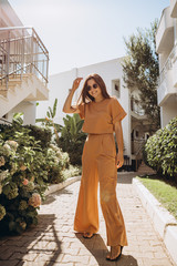 stylish young attractive woman wearing an orange-colored trouser suit and sunglasses photographed...