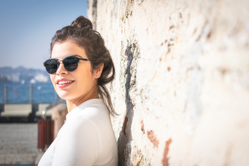 Attractive brunette girl in casual clothes is leaning to colorful rocky wall and looking sideway to the left with a black space on the right side. Out of focus foreground image.