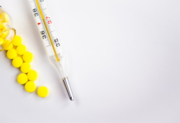 Mercury thermometer with temperature and a handful of yellow tablets on a light background. The concept of medicine.