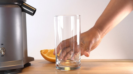 hand reaching to an empty glass next to a juicer and sliced orange