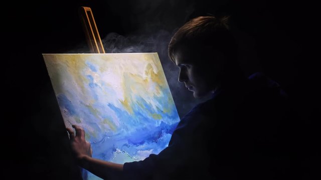 Artist copyist paint seascape with ship in ocean. Vaper smoke vape e-cigarette. Craftsman decorator draw as boat sail on blue sea with acrylic oil color. Draw finger, brush, knife palette. Indoor.