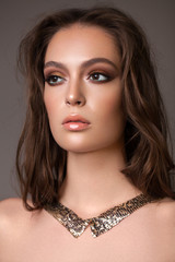 Portrait of young beautiful girl with professional makeup, gold eyeshadows, mint eyeliner and nude glossy lips.