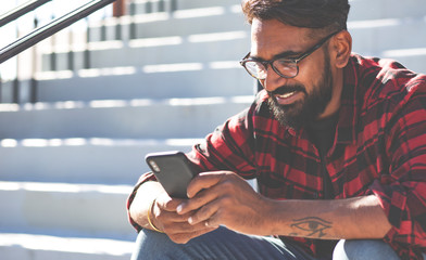 Handsome young man, outdoor. Indian man is texting a message on a cell phone.