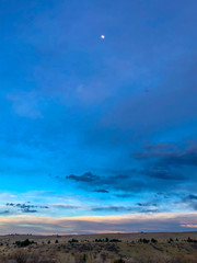 Obraz premium Dusk Moon in a blue sky over grasslands 