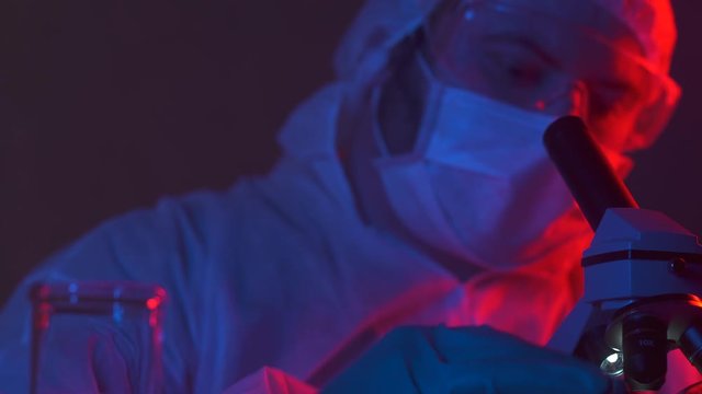Scientist in hazard suit in electronic manufacturing factory research new device. New silicon electronic chip in the hands of a researcher in a dark lablaboratory. Cyber technology development.