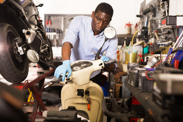 Male afro american worker repairing scooter in motorcycle workshop