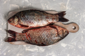 Two fresh crucian fish lies on a white wooden cutting board on a light gray background. Top view