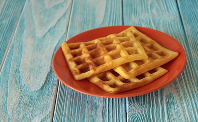 Fresh baked waffles on a plate on a blue wooden table.