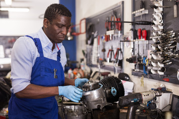 Afro american worker in overalls inspects a motorcycle engine