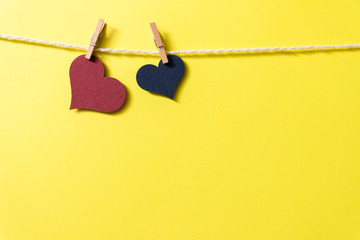 Two hearts on a rope hanging on tiny clothespins on a yellow background.