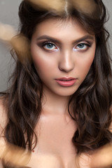 Close up photo of a beautiful young girl with professional makeup, gold eyeliner, graphic grey eyeshadows and curl hair.