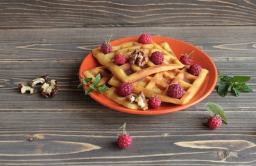 Homemade waffles with raspberries on an orange platter, on a wooden background.