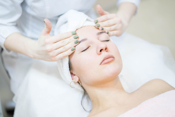 Woman in white and pink towel is having a face massage from a doctor cosmetologist in a white  uniform