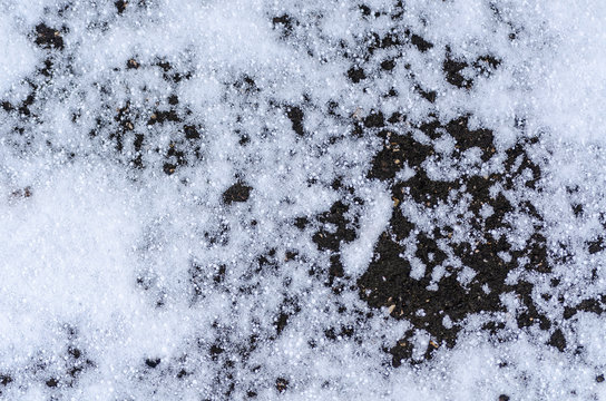 Texture of gray asphalt with melting snow in driveway. Concept of abstract rough scabrous surface of spring and winter season. Close-up of precipitation on road. Minimalistic design with copy space
