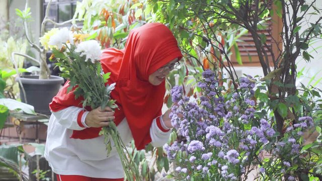 Happy senior woman smelling flower while holding some flower in home garden. Shot in 4k resolution