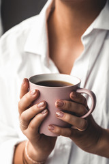 Woman in a white t-shirt holds morning coffee in a pink ceramic cup. Manicure. Front view