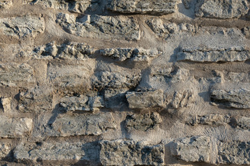 Fragment of a satar wall of gray flat stones. The masonry is connected by a gray cement composition. Background. Texture.