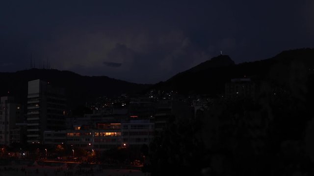 Lightning strikes behind the Corcovado mountain with the statue of Christ on top and city lights of Ipanema beach in the foreground