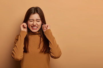 Distressed frustrated woman plugs ears, clenches teeth, hears bothering noise, avoids unpleasant...