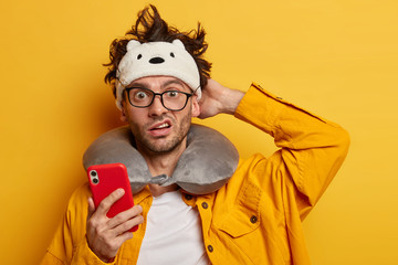 Indignant puzzled European man scratches head, reads news online via mobile phone, prepares for...