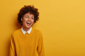 Portrait of pleasant looking overjoyed woman laughs and turns gaze aside, expresses good emotions...