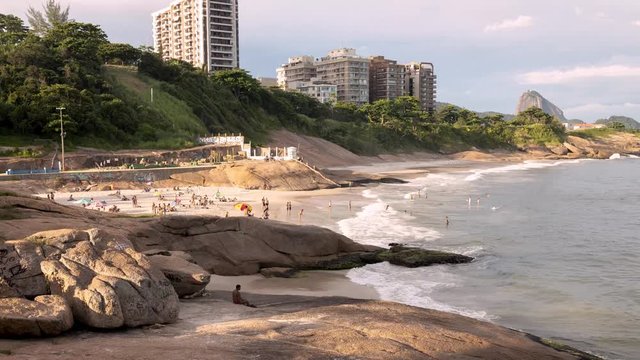 Motion time lapse pan showing part of the Arpoador rock in Ipanema and people enjoying the Devils beach with the Sugarloaf mountain and Copacabana fort in the background