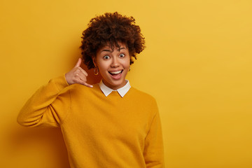 Cute young woman makes phone gesture, shows call me back sign, asks for telephone number, gestures...