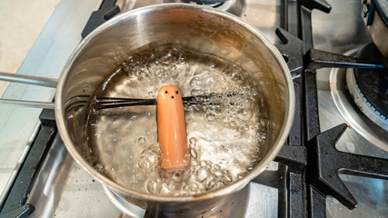 Sausage with eyes and spaghetti hair is cooked in a pan. Funny recipe.