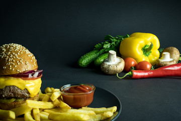 Hamburger with french fries and ketchup near organic vegetables on black background