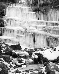 Black and white, beautiful, scenic, frozen Tupavica waterfall with hanging icicles and mountain creek with orange rocks and fallen leaves