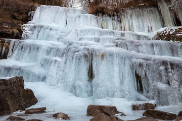 Beautiful, scenic, frozen Tupavica waterfall with hanging icicles and mountain creek with orange rocks and fallen leaves