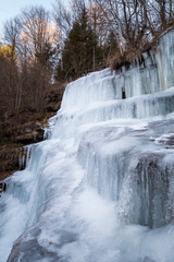 Beautiful, scenic, frozen Tupavica waterfall with hanging icicles and mountain creek with orange rocks and fallen leaves