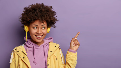 Pretty dark skinned woman with Afro hairstyle, points index finger on blank space, shows promo with...