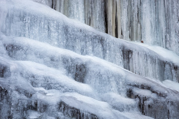 Amazing, close-up view of completely frozen waterfall, beautiful details of frozen water and icicles hanging from the cliff