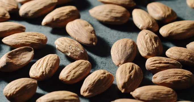 Many fresh almonds nuts rotating on dark kitchen surface. Close up macro shot of almond. 