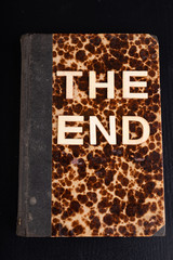 The words the end arranged from wooden letters on the background of the old book. Old-style text n the table.